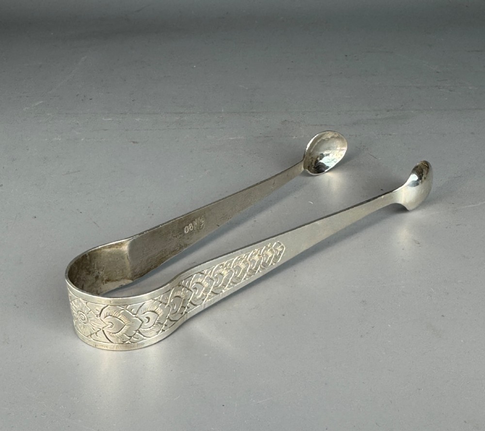 A pair of silver sugar tongs featuring textured engraved decoration near the arch and spoon-shaped bowls. View IV