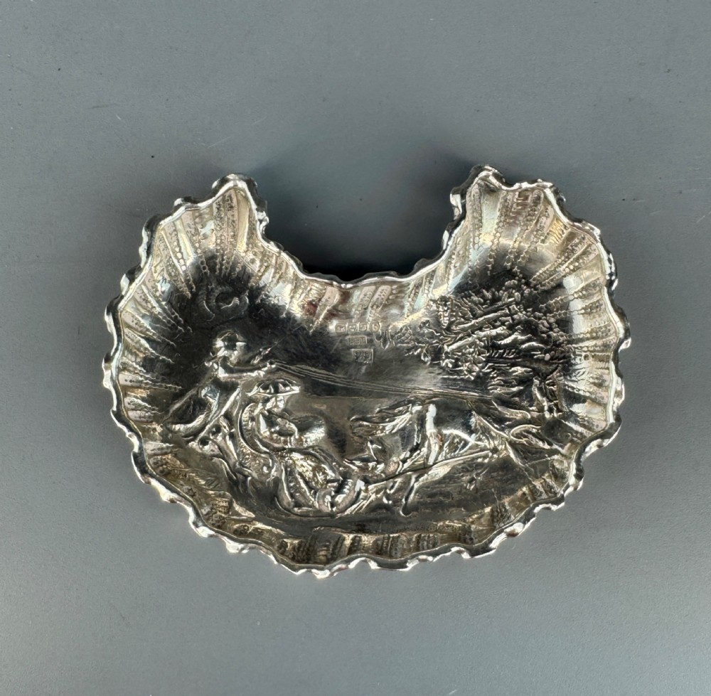 A late Victorian crescent-shaped sterling silver trinket dish with embossed repousse figural scenes and a fluted border.