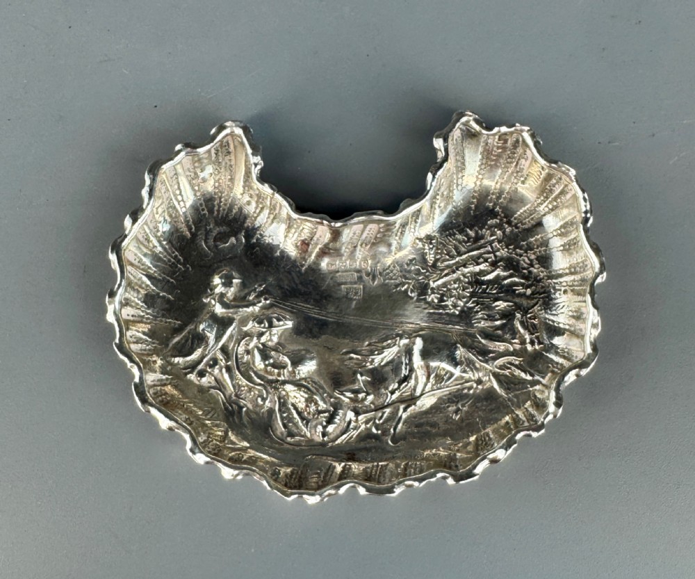 A late Victorian crescent-shaped sterling silver trinket dish with embossed repousse figural scenes and a fluted border. View V