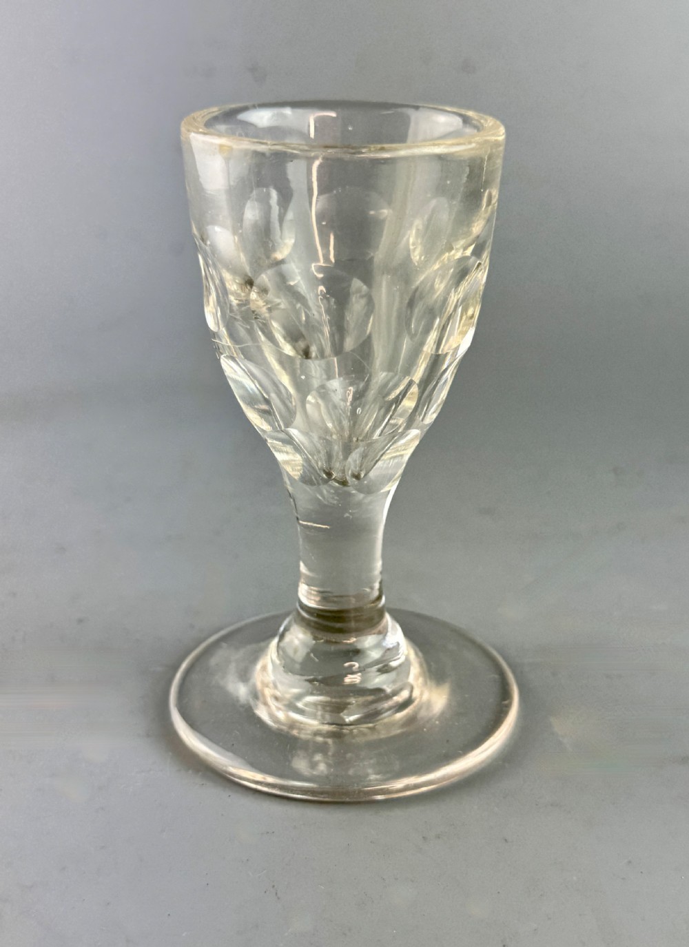 A clear Victorian glass featuring thumb-cut facets around the lower bowl, a short solid stem, and a wide flat base.