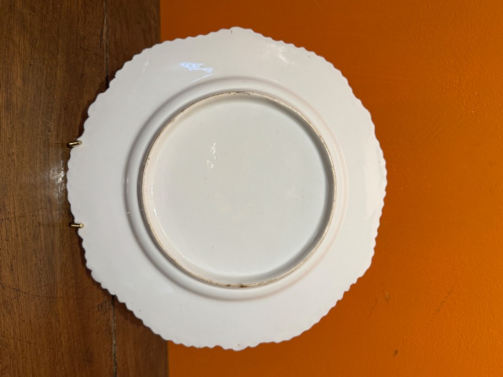 An early 19th-century circular porcelain cabinet plate featuring a pink ground, scalloped gold rim, hand-painted central sunflower, and surrounding floral cartouches with gilt detailing. View II