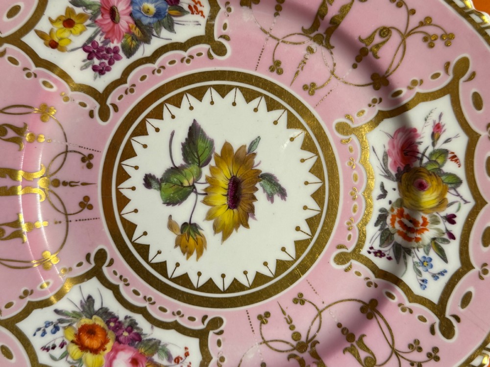 An early 19th-century circular porcelain cabinet plate featuring a pink ground, scalloped gold rim, hand-painted central sunflower, and surrounding floral cartouches with gilt detailing. View III