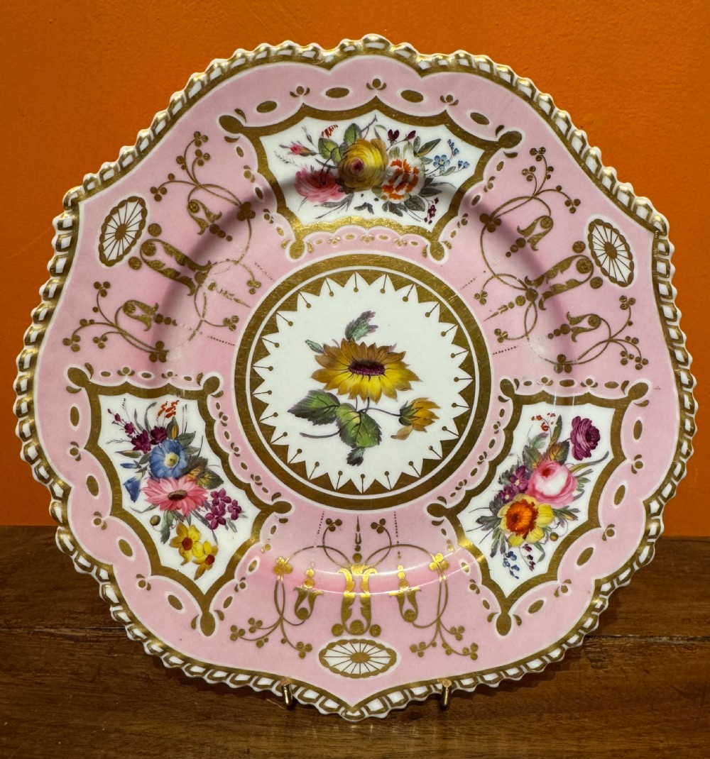 An early 19th-century circular porcelain cabinet plate featuring a pink ground, scalloped gold rim, hand-painted central sunflower, and surrounding floral cartouches with gilt detailing. View V