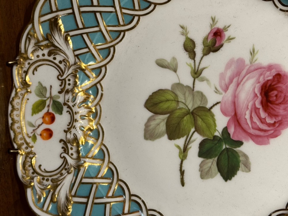 A circular Victorian Minton porcelain plate featuring a central hand-painted pink rose surrounded by a turquoise basketweave border and gilded scroll cartouches displaying fruit motifs. View II