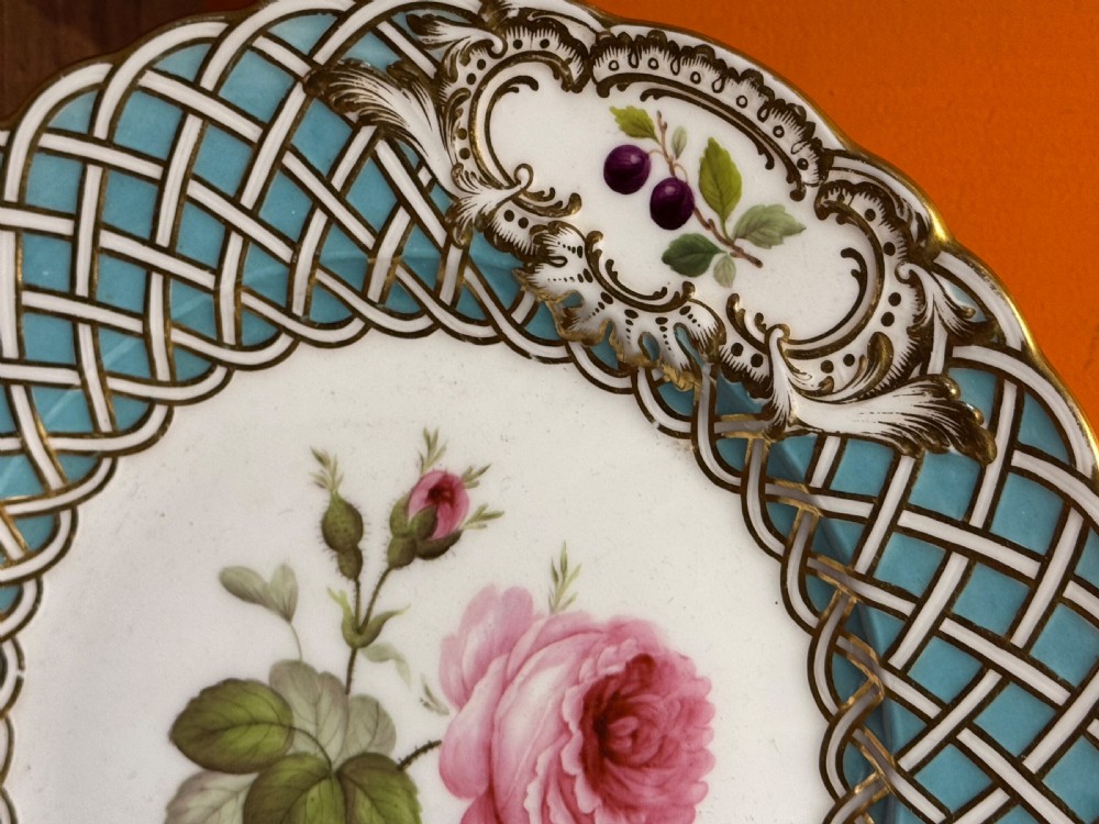 A circular Victorian Minton porcelain plate featuring a central hand-painted pink rose surrounded by a turquoise basketweave border and gilded scroll cartouches displaying fruit motifs. View IV