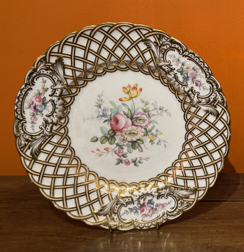 A circular Minton porcelain plate featuring a gilded basketweave border, rococo scroll cartouches, and hand-painted central floral bouquet on a white background.