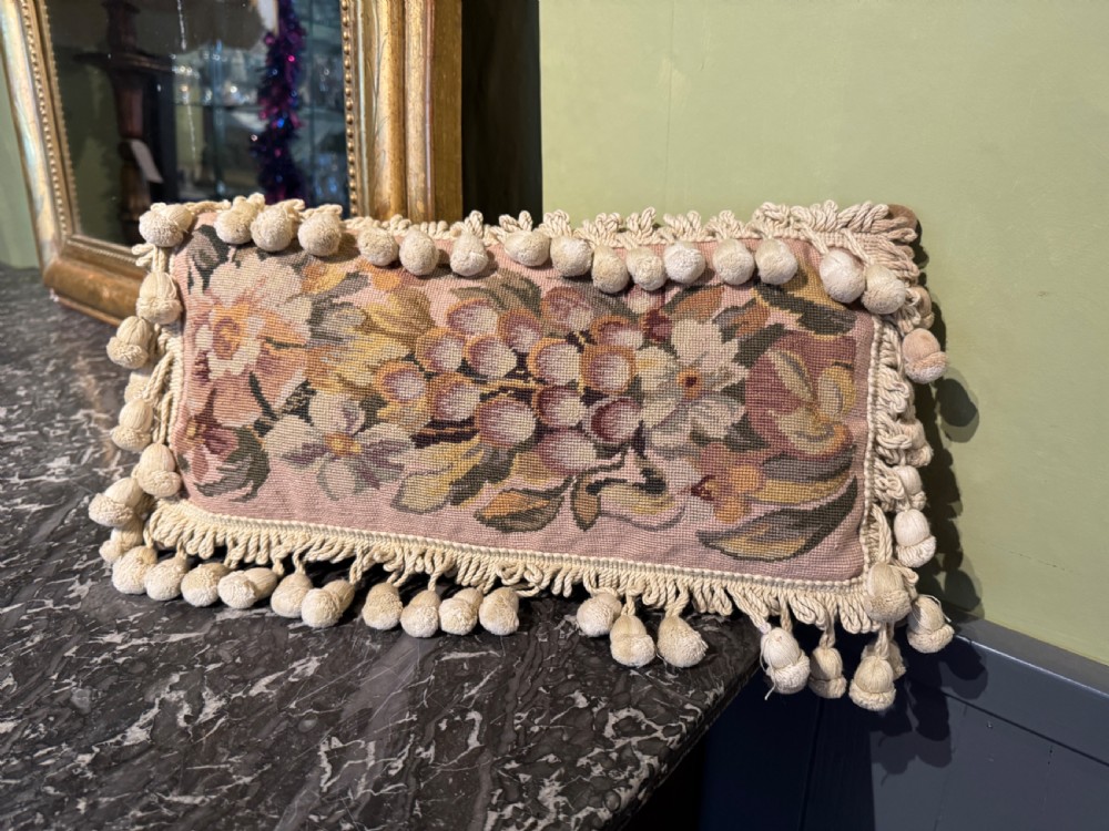 A rectangular antique French tapestry cushion with floral needlepoint detail in beige and pink tones, trimmed with a fringe and pom-pom border. View III