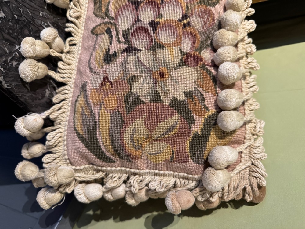 A rectangular antique French tapestry cushion with floral needlepoint detail in beige and pink tones, trimmed with a fringe and pom-pom border. View IV