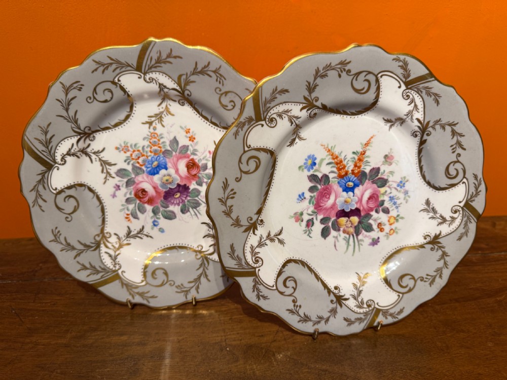 A pair of Victorian Coalport porcelain dessert plates featuring scalloped gilded rims, grey borders with gold foliage, and central hand-painted floral bouquets.