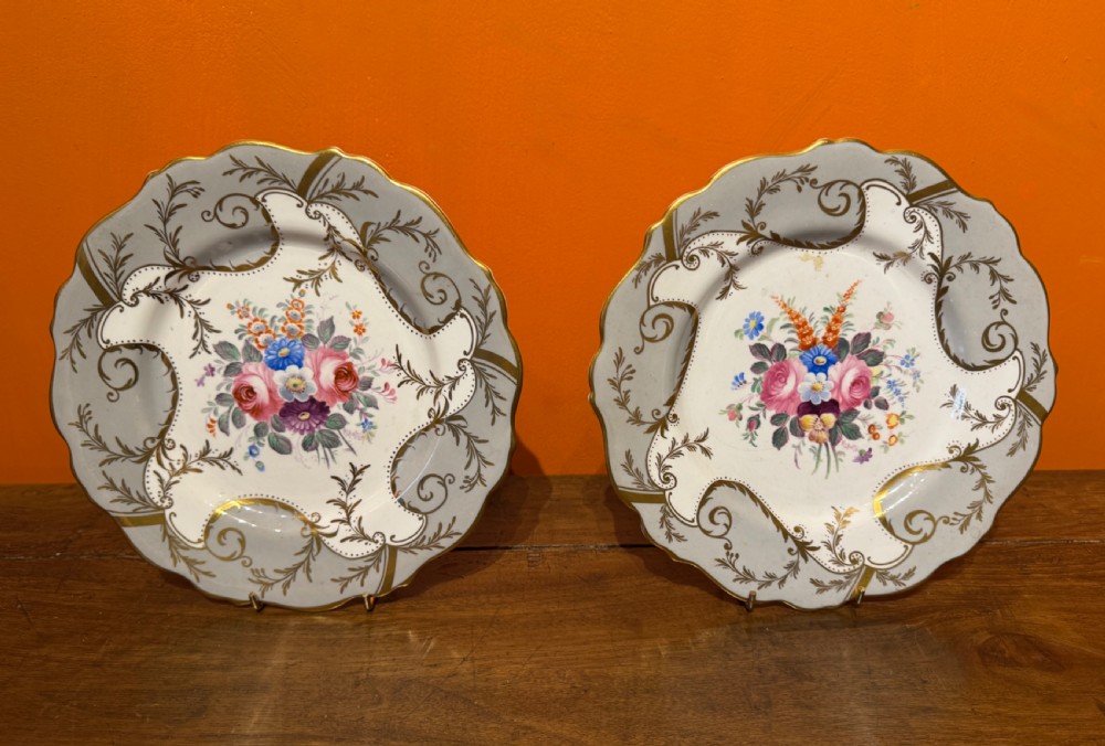 A pair of Victorian Coalport porcelain dessert plates featuring scalloped gilded rims, grey borders with gold foliage, and central hand-painted floral bouquets. View II