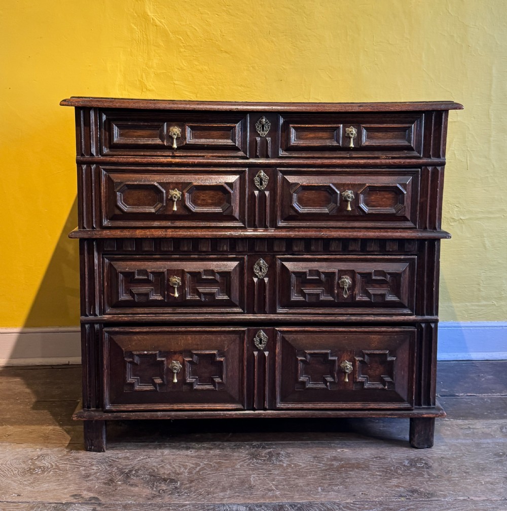 A 17th-century Charles II dark oak two-part chest of drawers featuring geometric mitred drawer mouldings and brass teardrop handles.