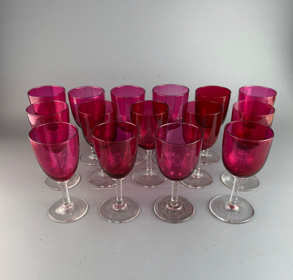 A set of fifteen Victorian wine glasses featuring cranberry-coloured glass bowls set upon clear glass stems and circular bases.