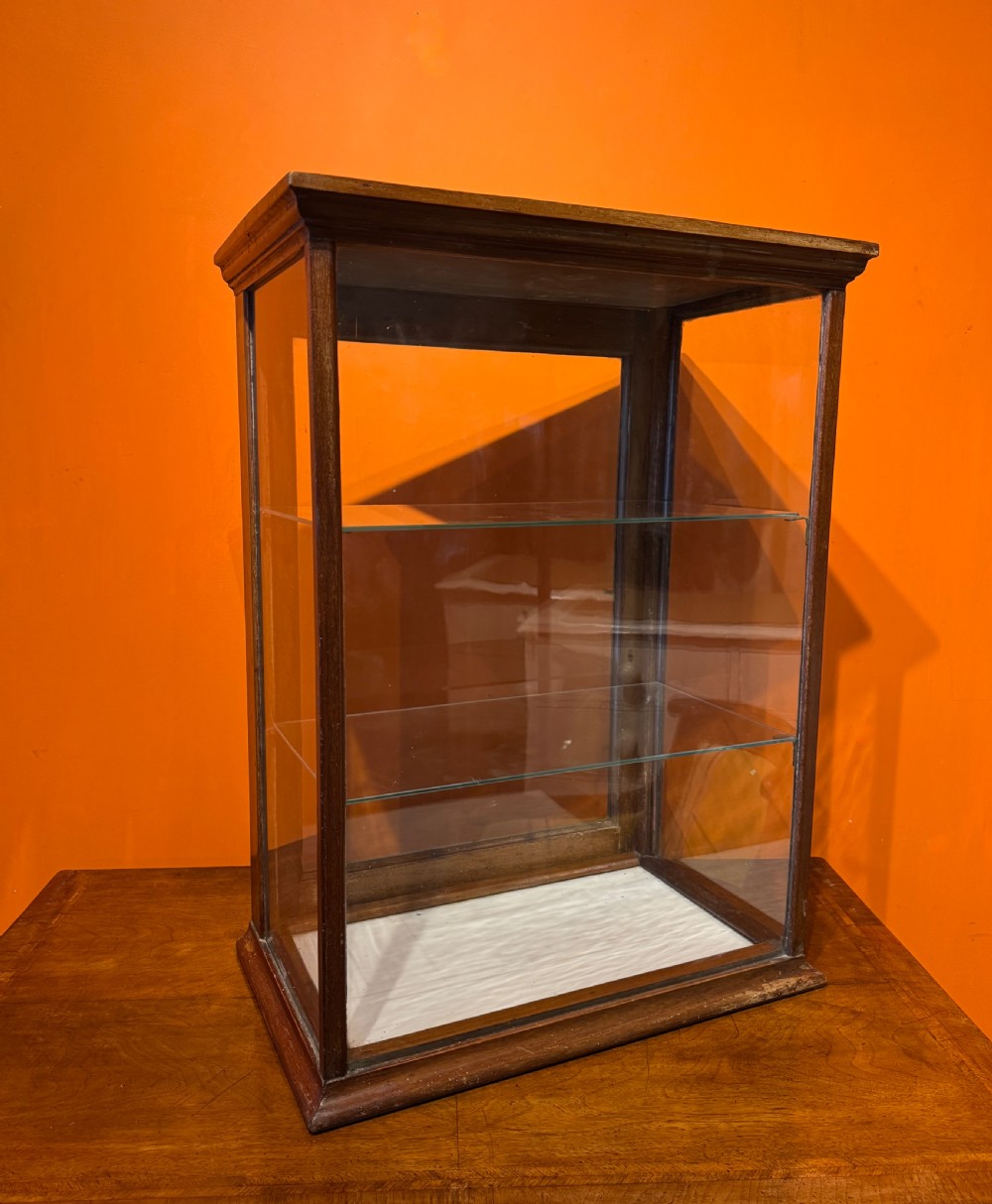 An Edwardian tabletop display cabinet featuring a mahogany frame with clear glass panels on all sides and two interior glass shelves.