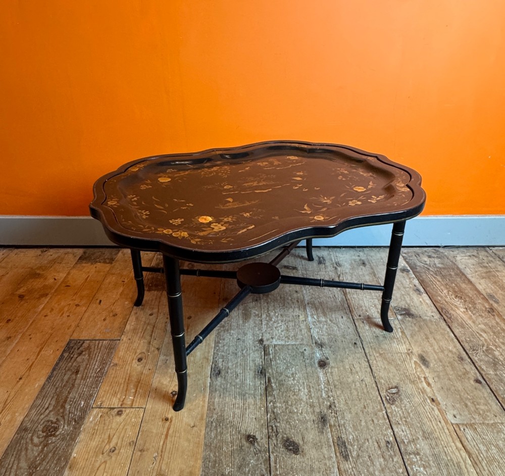 A Victorian ebonised papier-mache tray with serpentine edges and gilt Chinoiserie decoration, resting upon a turned black stand with faux bamboo legs. View II