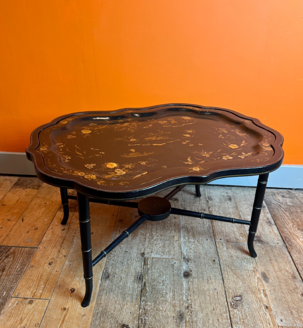 A Victorian ebonised papier-mache tray with serpentine edges and gilt Chinoiserie decoration, resting upon a turned black stand with faux bamboo legs. View VI