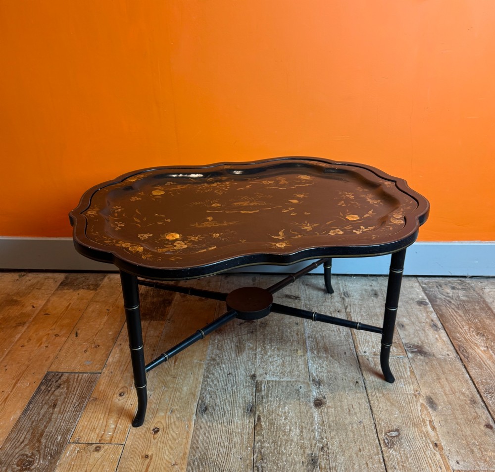 A Victorian ebonised papier-mache tray with serpentine edges and gilt Chinoiserie decoration, resting upon a turned black stand with faux bamboo legs. View VII