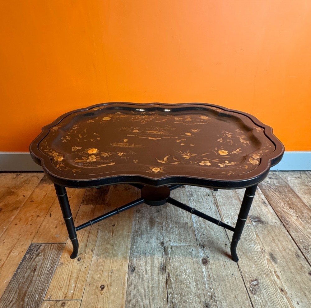 A Victorian ebonised papier-mache tray with serpentine edges and gilt Chinoiserie decoration, resting upon a turned black stand with faux bamboo legs. View VIII
