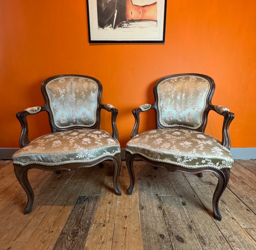 A pair of Louis XV style walnut fauteuil armchairs upholstered in sage green floral silk damask fabric featuring carved cabriole legs.