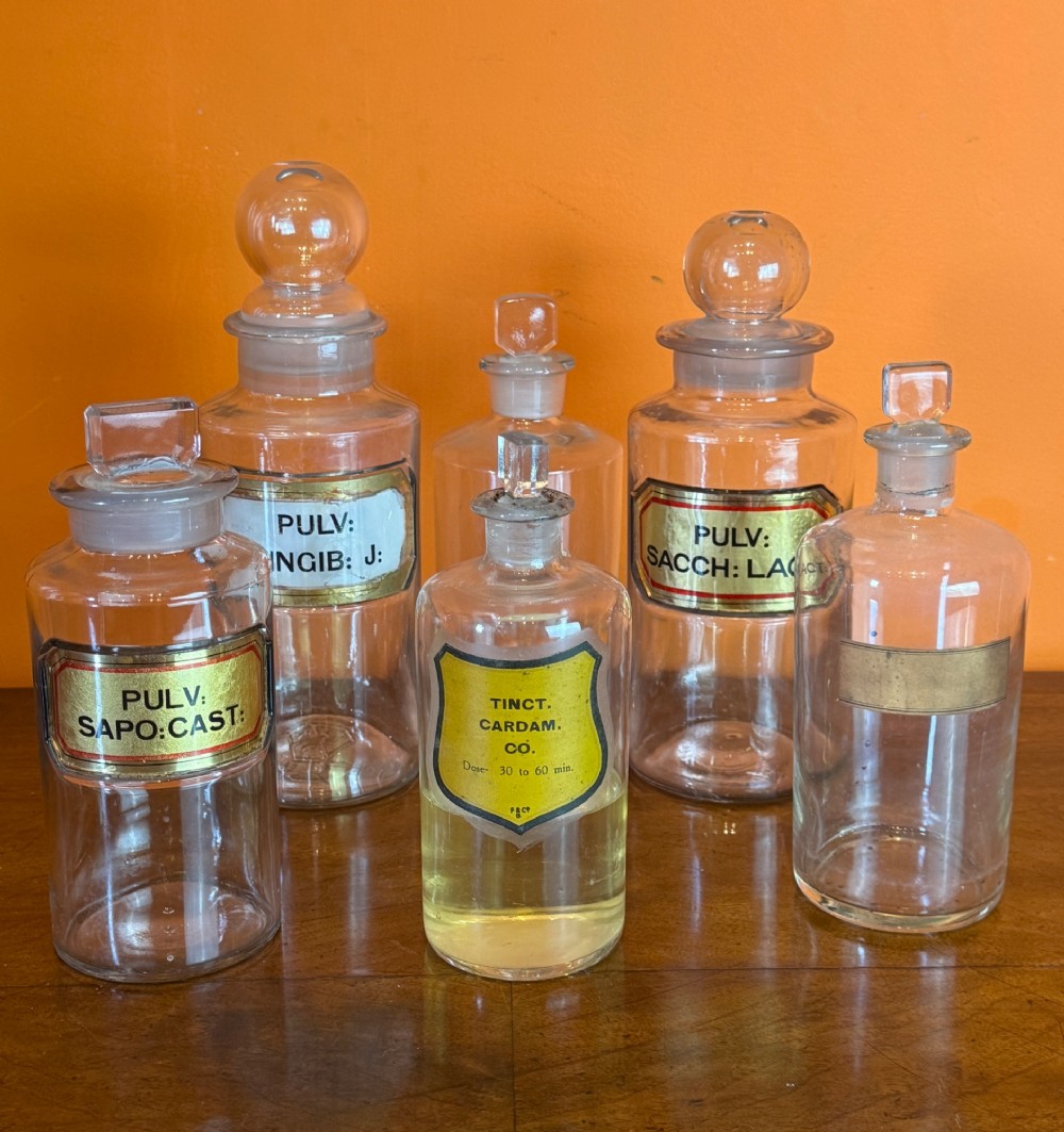 A collection of clear glass antique chemist bottles featuring ground glass stoppers and Latin apothecary labels trimmed in gold. View II
