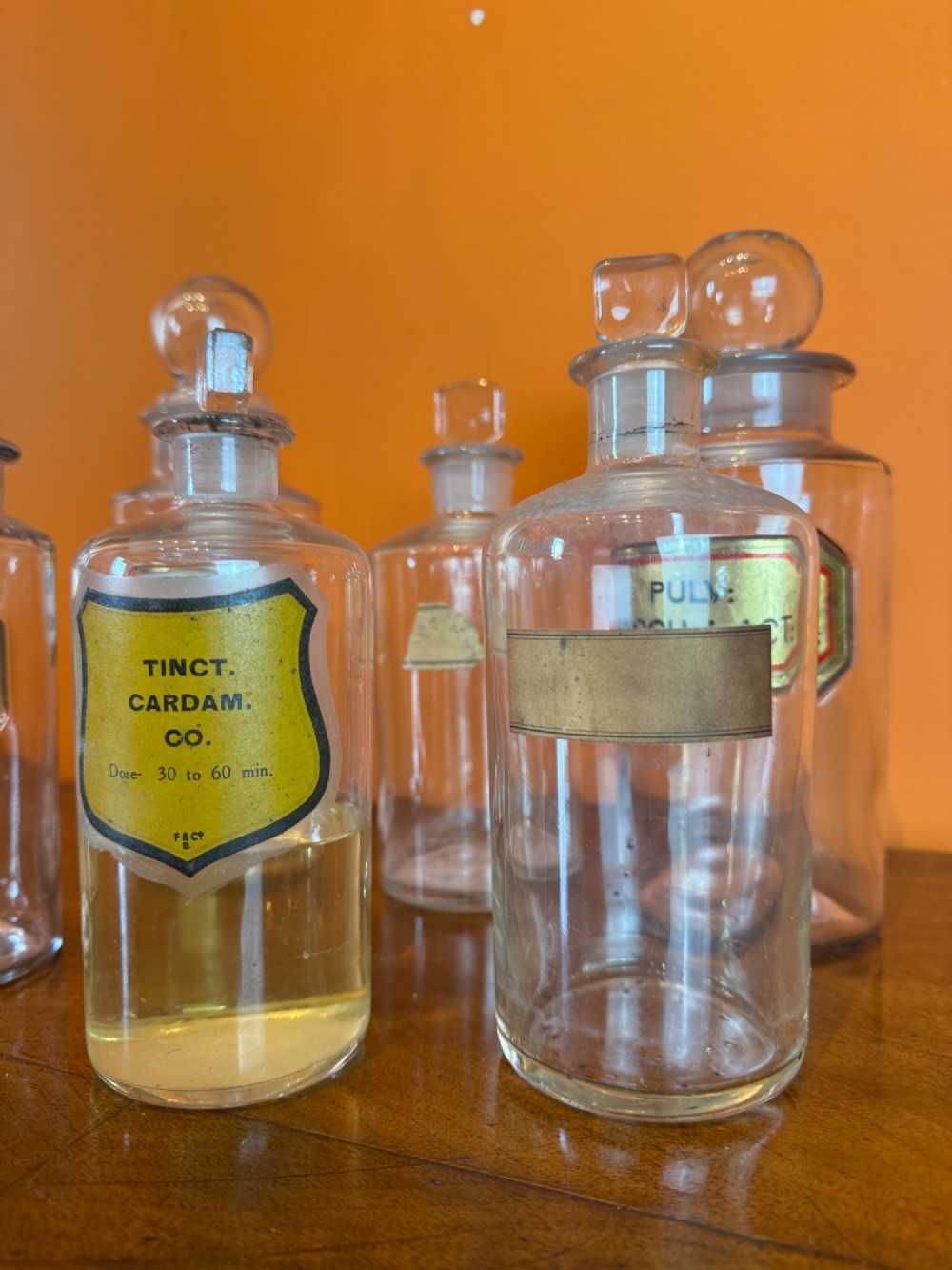 A collection of clear glass antique chemist bottles featuring ground glass stoppers and Latin apothecary labels trimmed in gold. View III