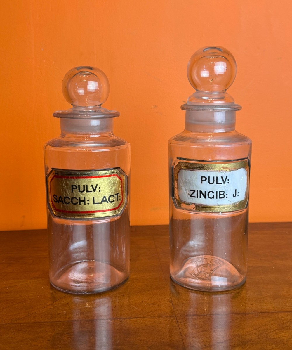 A collection of clear glass antique chemist bottles featuring ground glass stoppers and Latin apothecary labels trimmed in gold. View IV