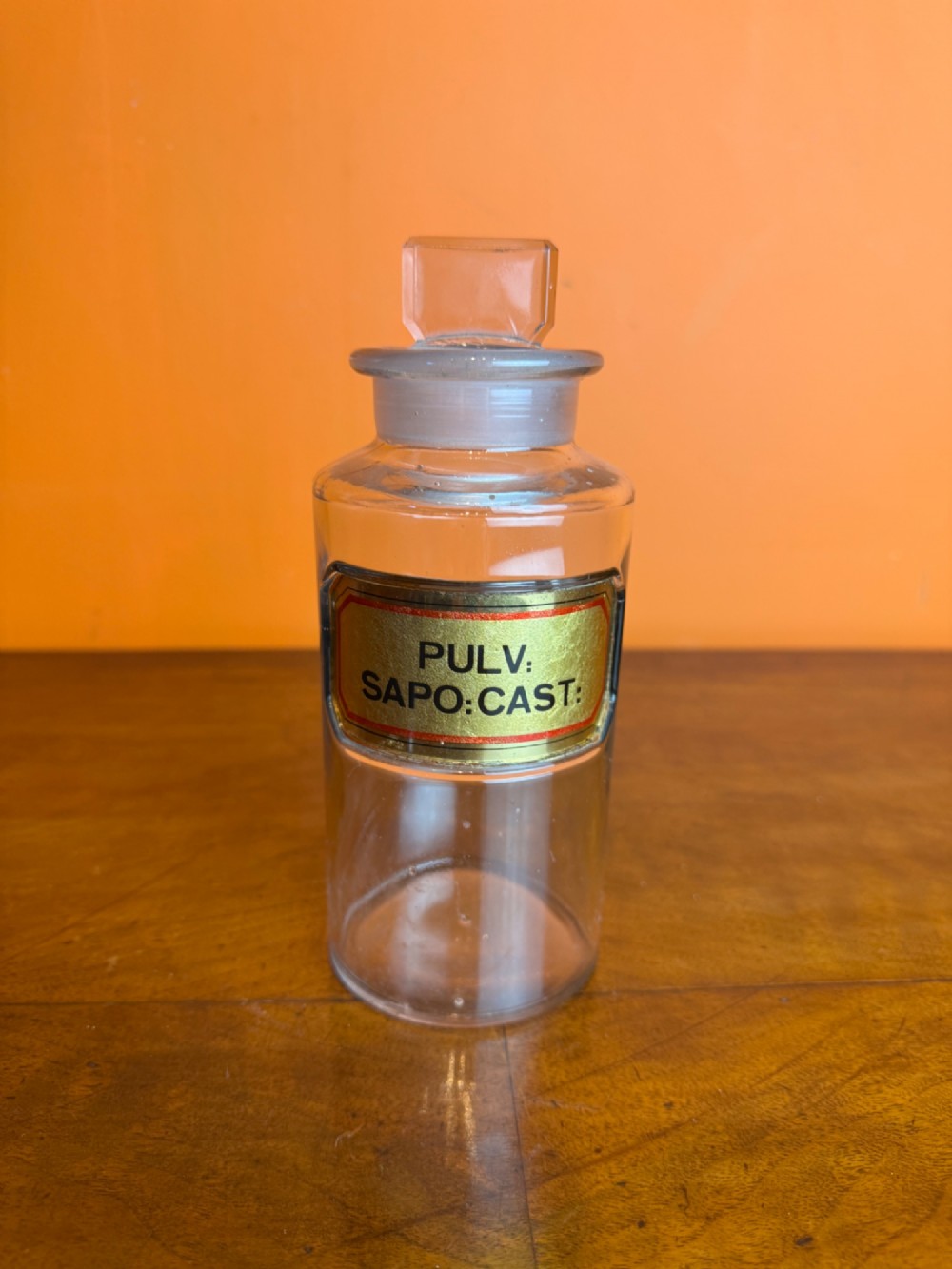 A collection of clear glass antique chemist bottles featuring ground glass stoppers and Latin apothecary labels trimmed in gold. View V