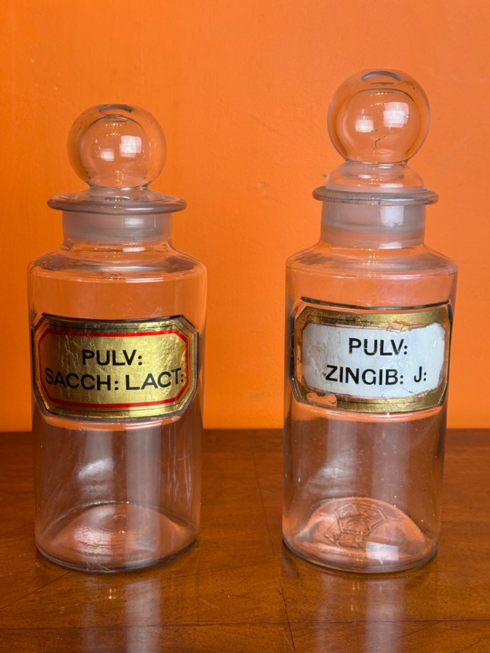 A collection of clear glass antique chemist bottles featuring ground glass stoppers and Latin apothecary labels trimmed in gold. View VIII