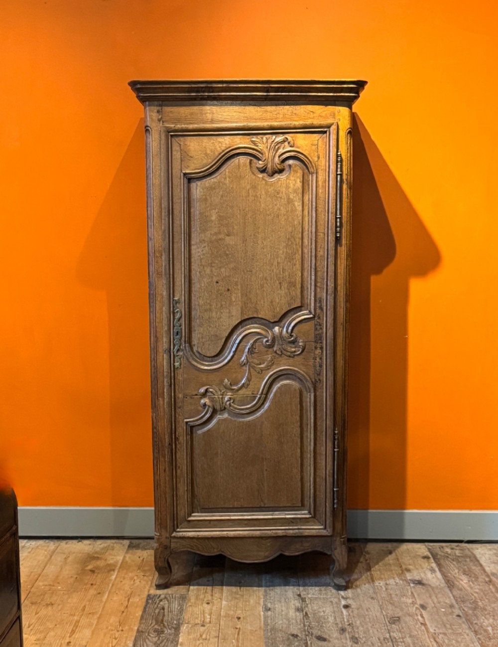 A 19th-century French oak bonnetiere featuring a single door with Louis XV style carved foliate mouldings, long iron hinges, and cabriole feet.