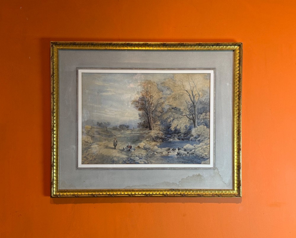 Framed landscape watercolour depicting figures beside a river with trees, presented in a cloth mount and a molded gilt frame.