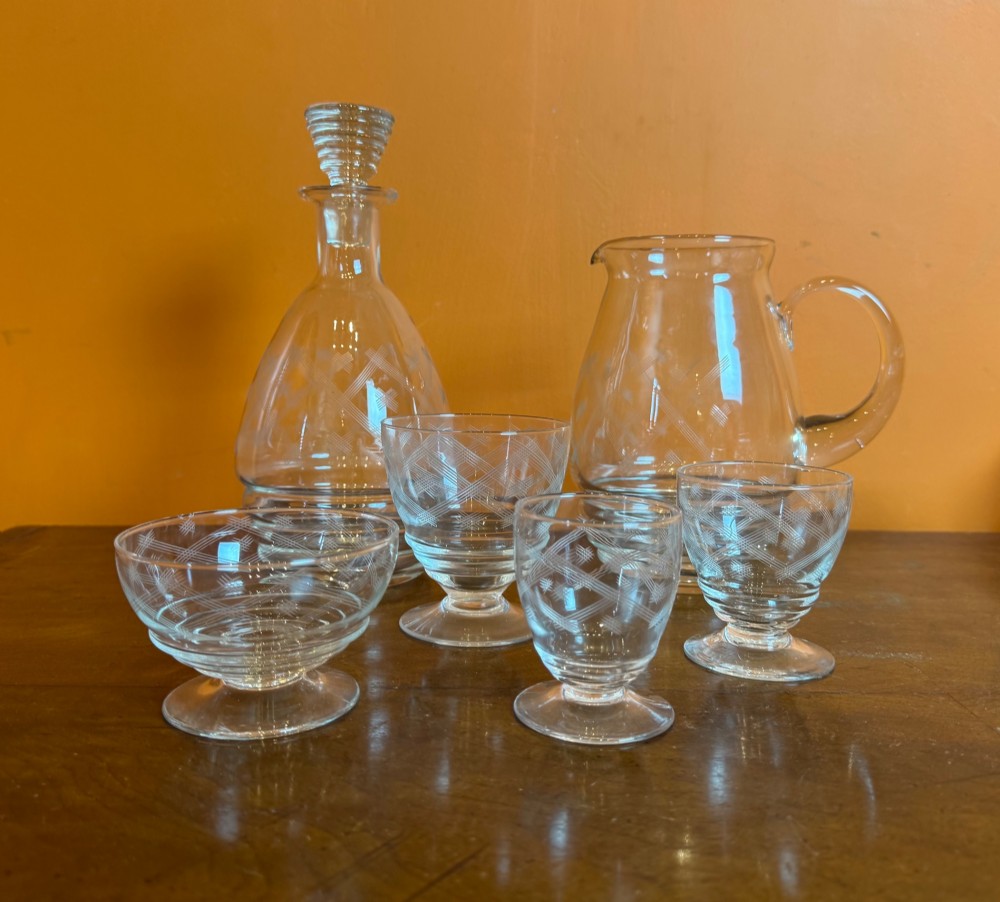 A 34-piece clear glass drinkware suite featuring engraved geometric motifs, including a stoppered decanter, water pitcher, stemware, and dessert bowls. View IV
