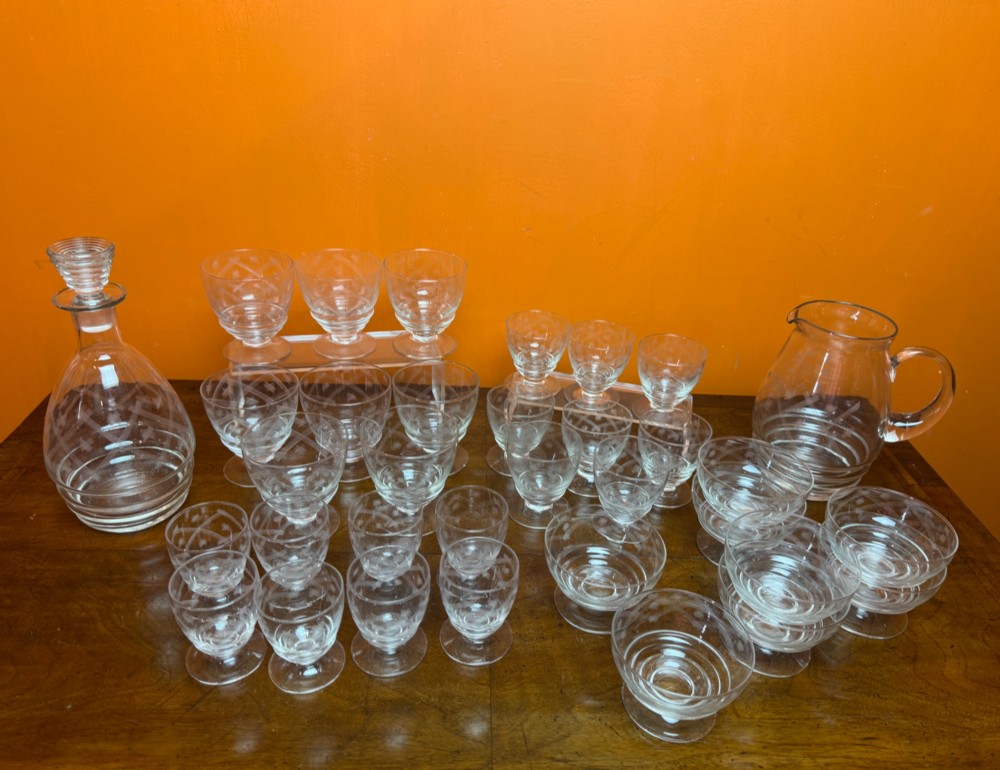 A 34-piece clear glass drinkware suite featuring engraved geometric motifs, including a stoppered decanter, water pitcher, stemware, and dessert bowls. View V