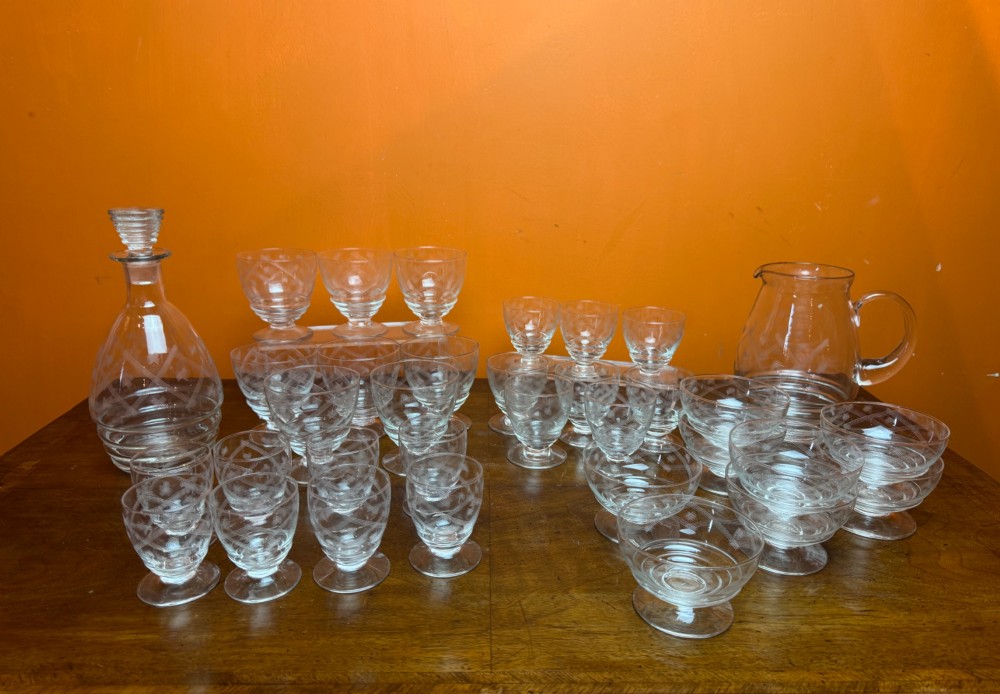 A 34-piece clear glass drinkware suite featuring engraved geometric motifs, including a stoppered decanter, water pitcher, stemware, and dessert bowls. View VII