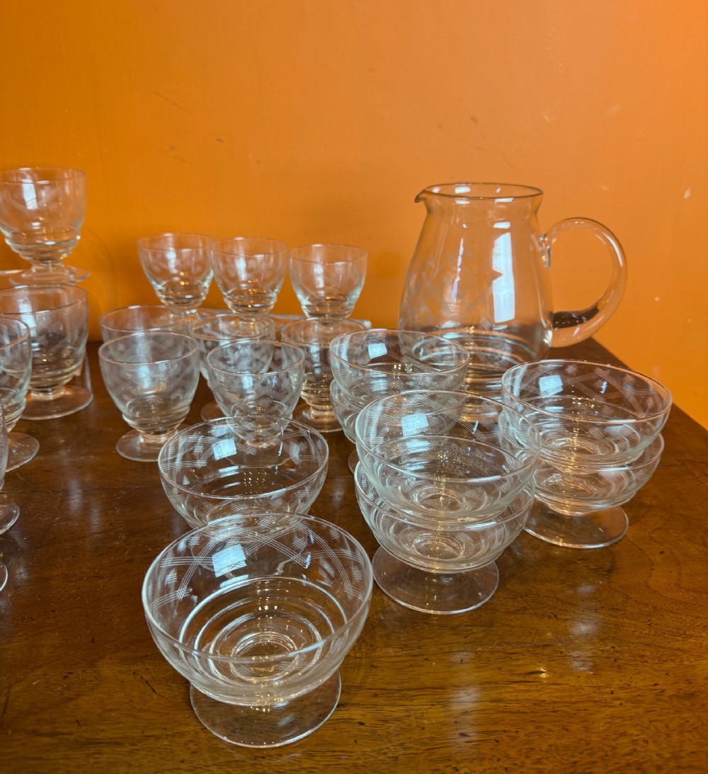 A 34-piece clear glass drinkware suite featuring engraved geometric motifs, including a stoppered decanter, water pitcher, stemware, and dessert bowls. View VIII