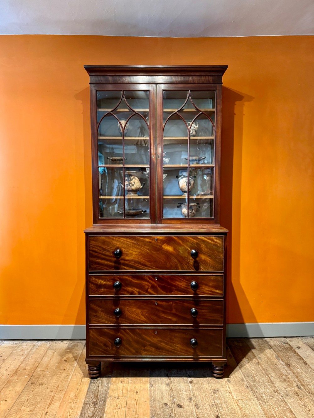 An antique Regency mahogany secretaire bookcase featuring upper Gothic astragal glazed doors over a lower chest of drawers on turned feet.