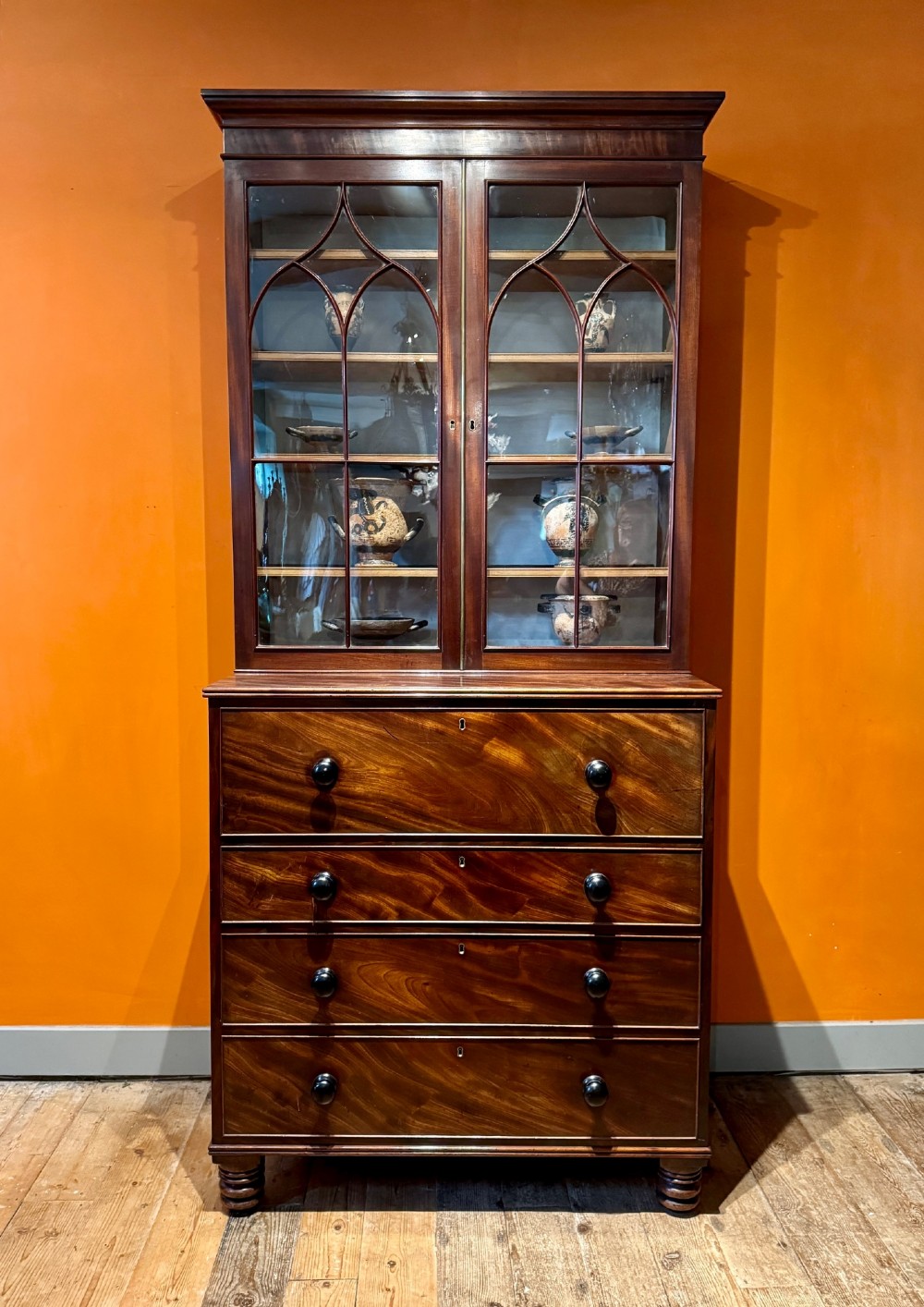 An antique Regency mahogany secretaire bookcase featuring upper Gothic astragal glazed doors over a lower chest of drawers on turned feet. View II