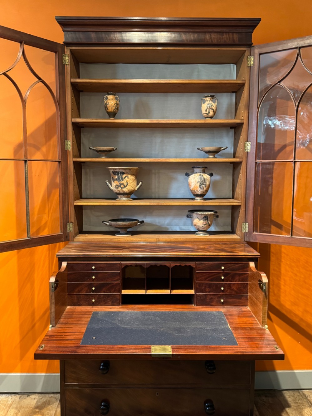 An antique Regency mahogany secretaire bookcase featuring upper Gothic astragal glazed doors over a lower chest of drawers on turned feet. View VI