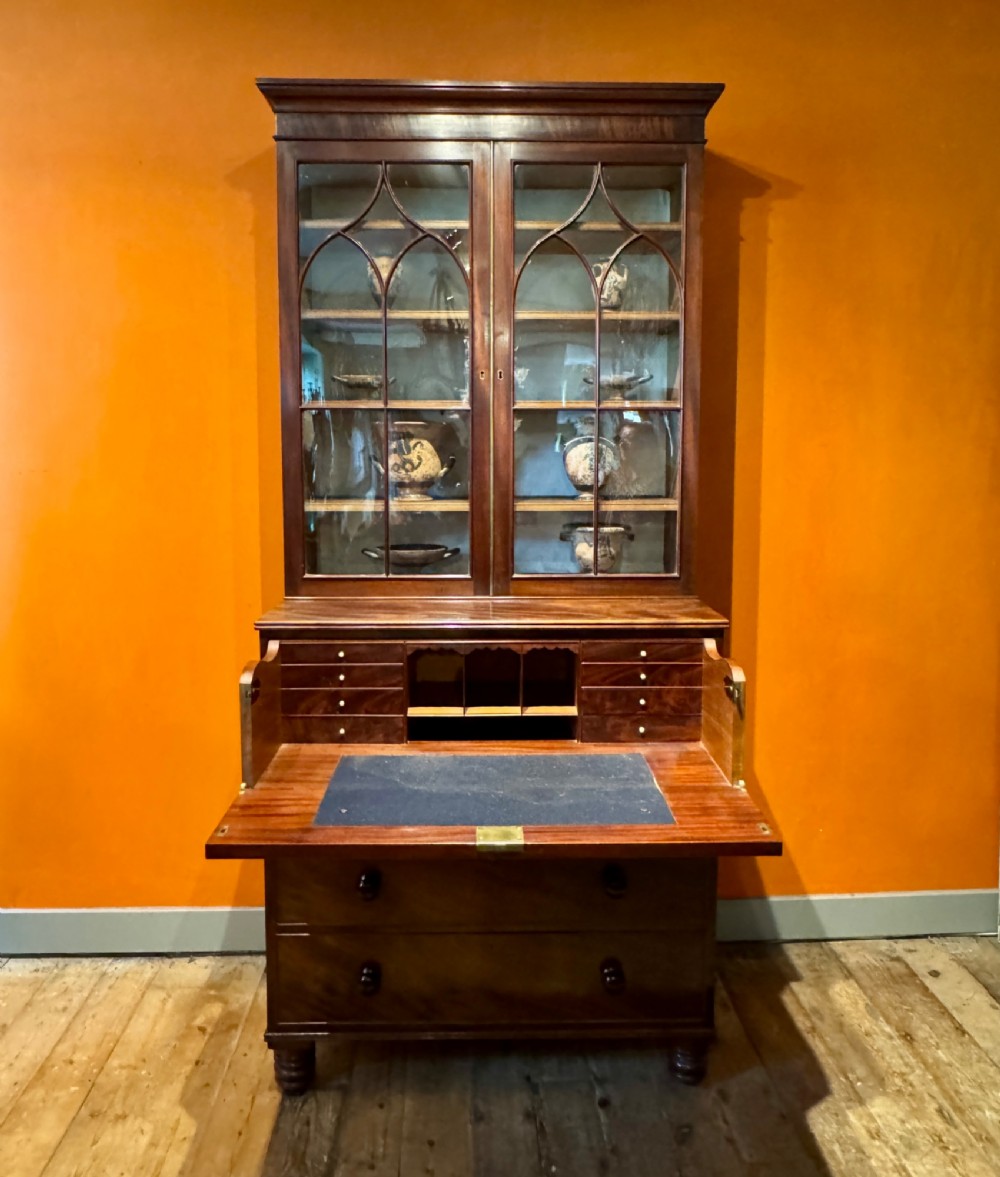 An antique Regency mahogany secretaire bookcase featuring upper Gothic astragal glazed doors over a lower chest of drawers on turned feet. View X
