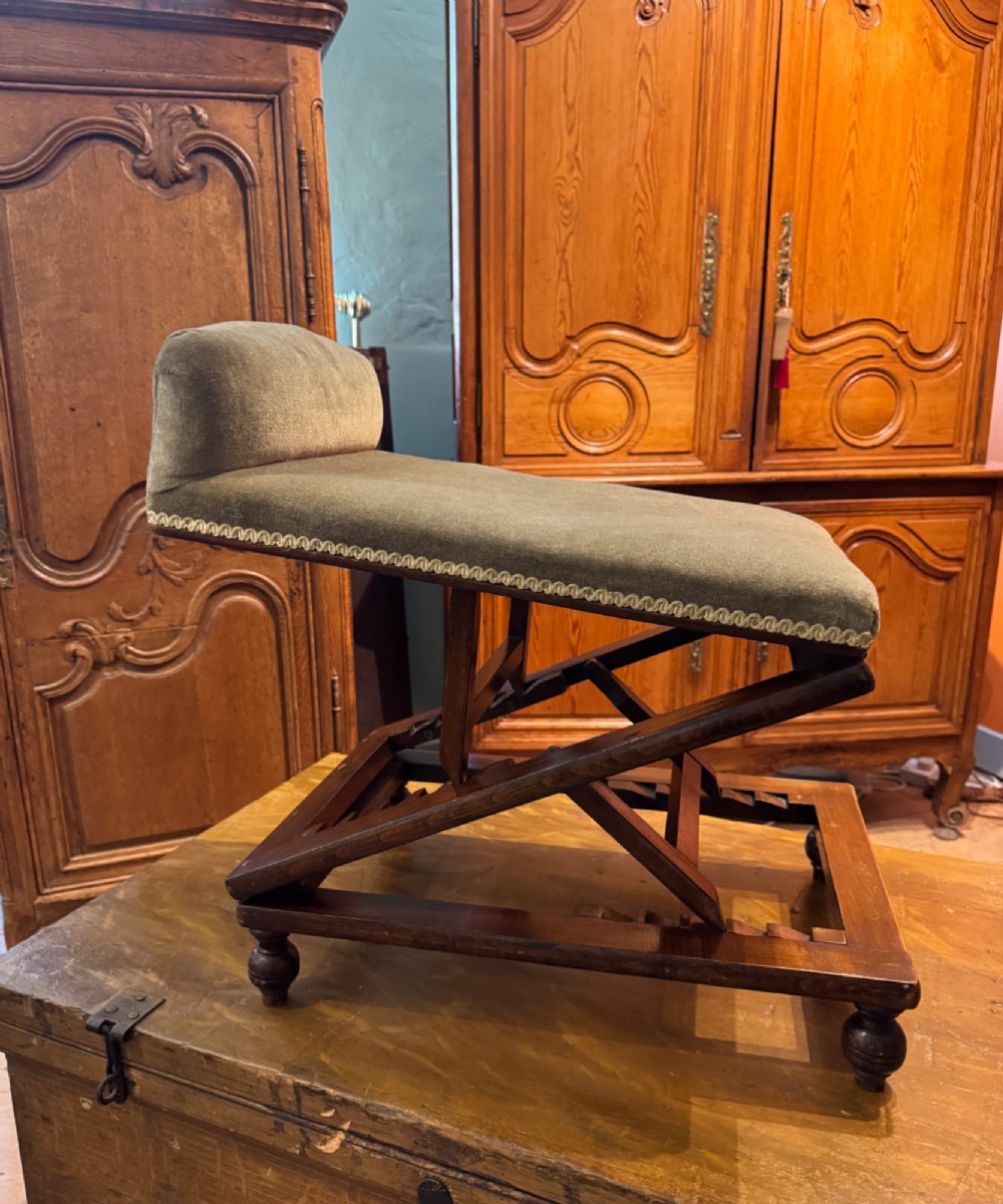 An antique Victorian metamorphic gout stool with a dark stained beech ratchet frame and an inclined green velvet upholstered cushion. View II