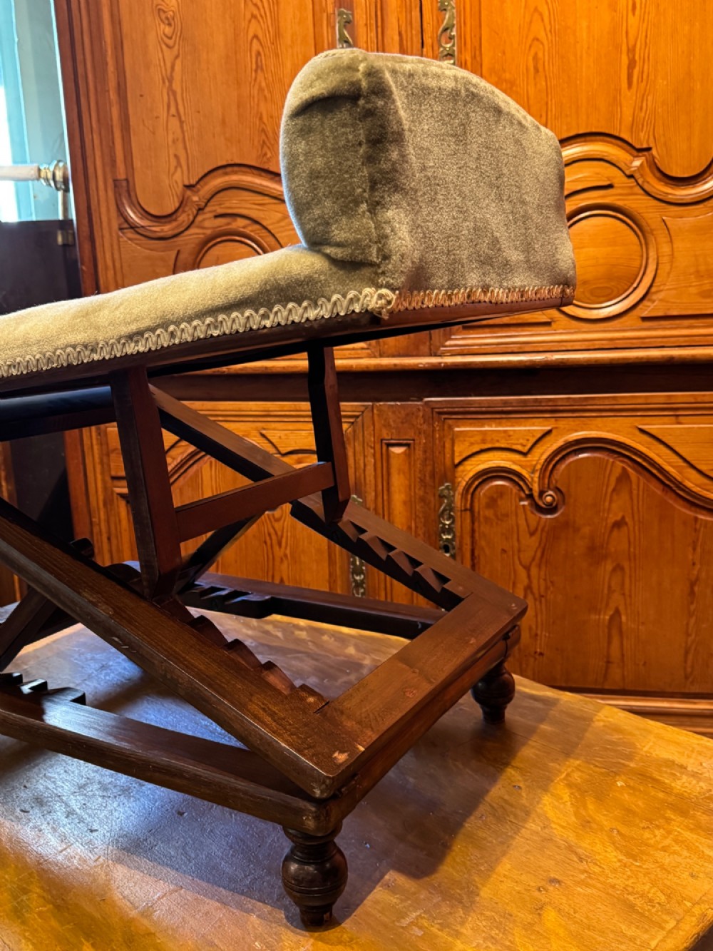 An antique Victorian metamorphic gout stool with a dark stained beech ratchet frame and an inclined green velvet upholstered cushion. View VI