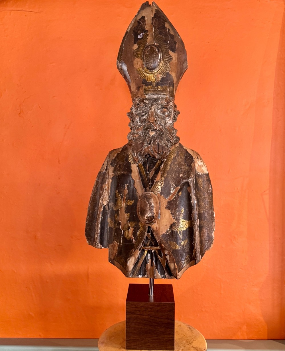 An eighteenth-century carved gilt-wood bust of a bearded bishop wearing a mitre, showing distressed gilding and mounted on a dark wooden block base.