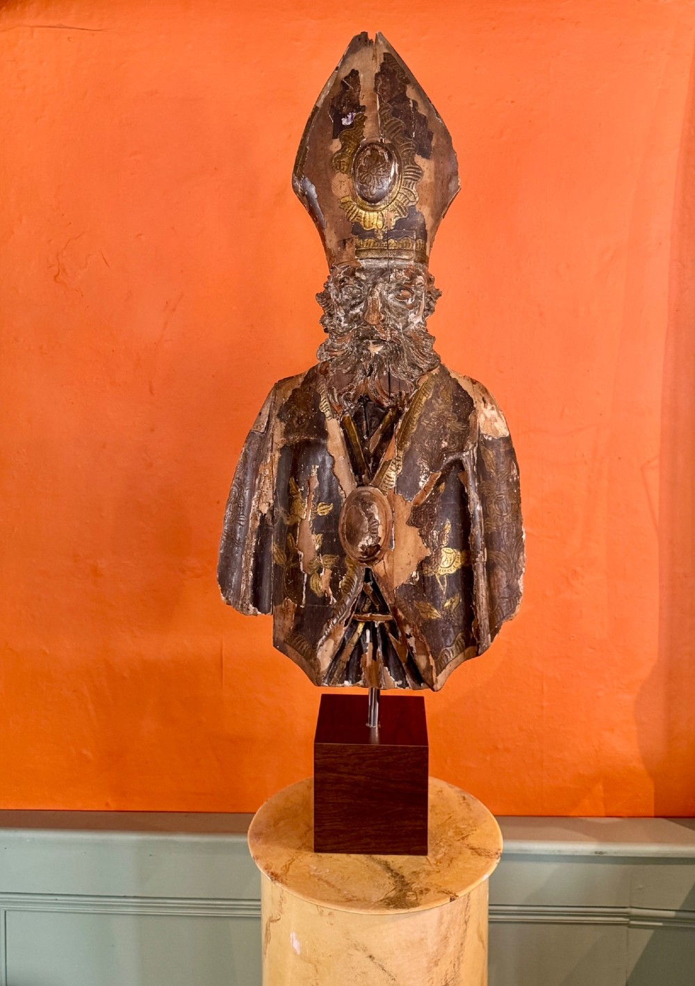 An eighteenth-century carved gilt-wood bust of a bearded bishop wearing a mitre, showing distressed gilding and mounted on a dark wooden block base. View II