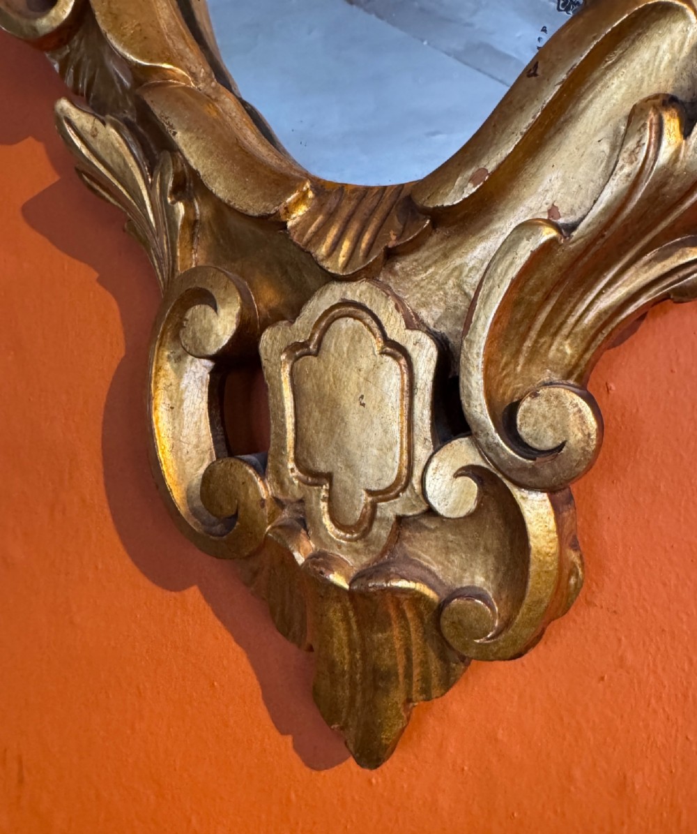 An Italian Rococo carved giltwood wall mirror with an ornate C-scroll frame and an engraved mirror plate displaying a musical instrument motif. View III