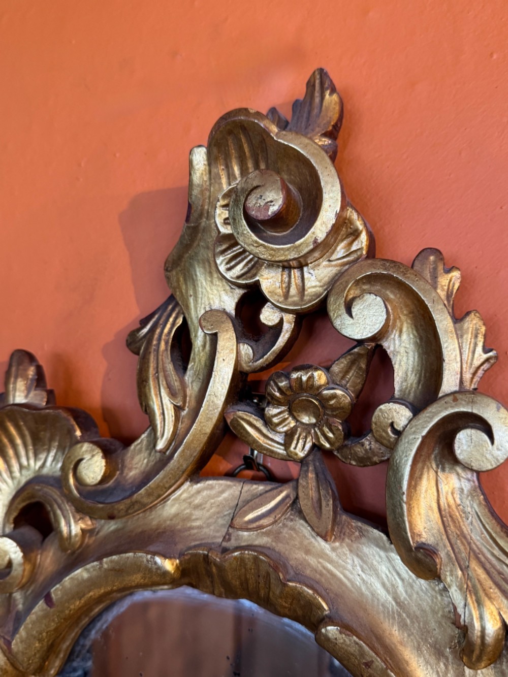 An Italian Rococo carved giltwood wall mirror with an ornate C-scroll frame and an engraved mirror plate displaying a musical instrument motif. View IV