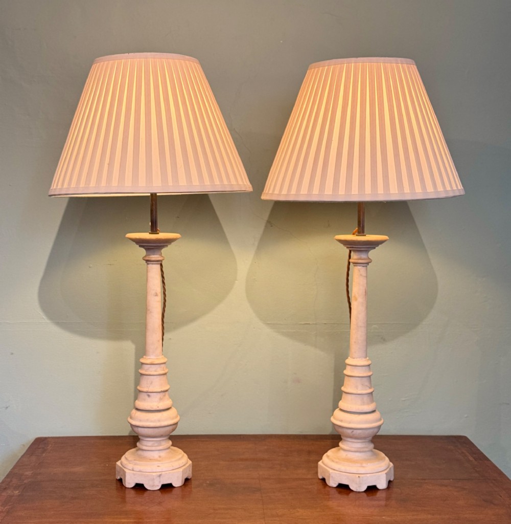 A pair of turned off-white marble table lamps featuring cylindrical baluster shafts, stepped circular bases, and cream pleated fabric shades. View II