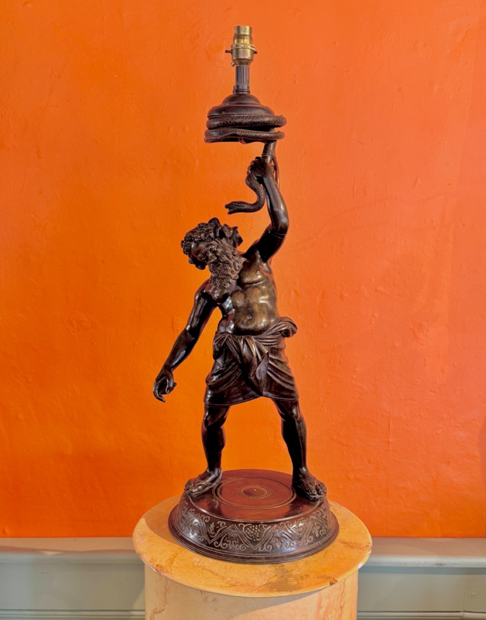 A dark patinated bronze sculptural table lamp depicting the classical figure Silenus holding a coiled serpent, set upon a carved circular base. View II