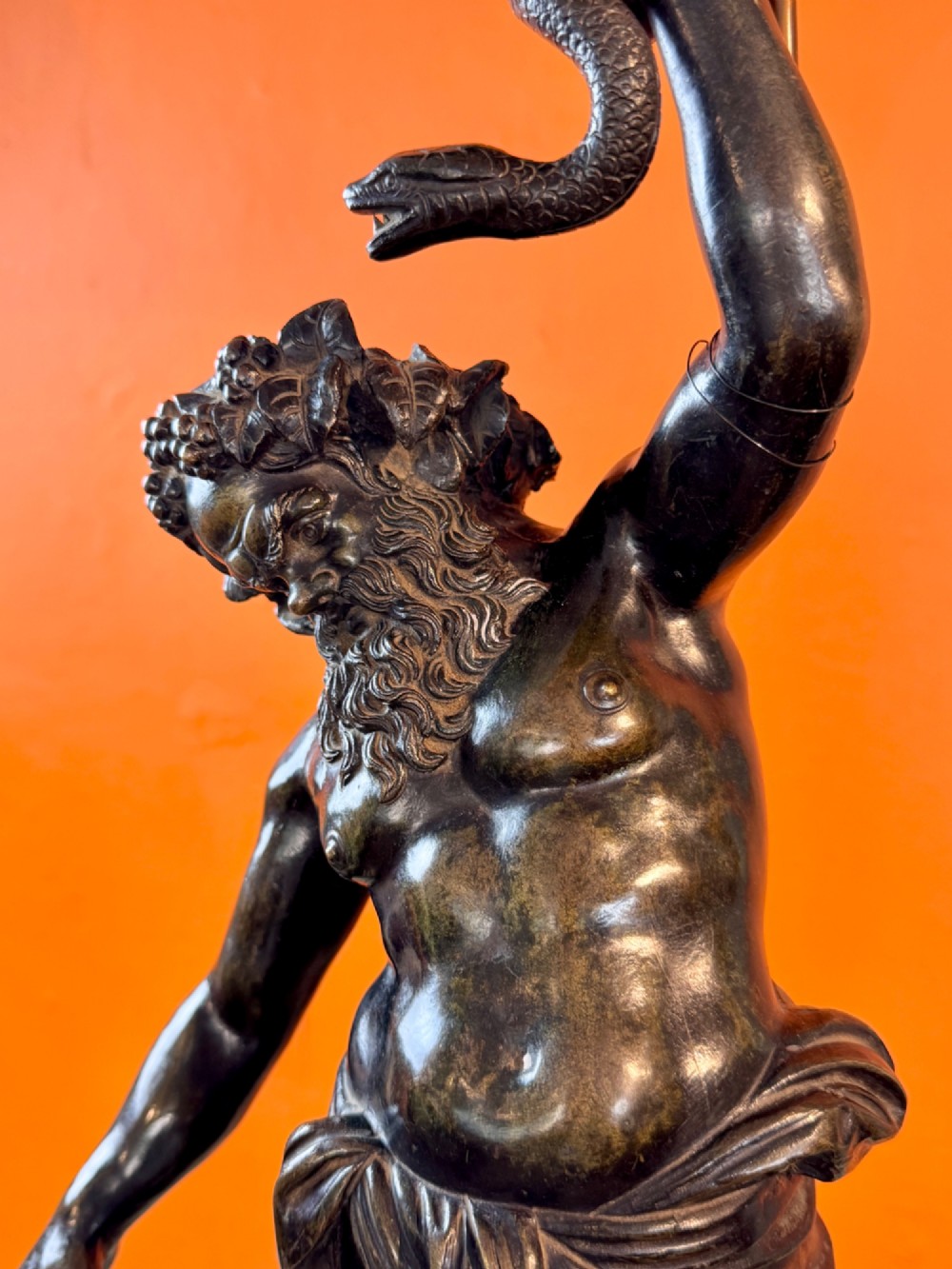 A dark patinated bronze sculptural table lamp depicting the classical figure Silenus holding a coiled serpent, set upon a carved circular base. View IV