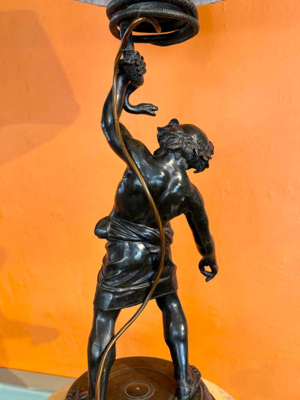 A dark patinated bronze sculptural table lamp depicting the classical figure Silenus holding a coiled serpent, set upon a carved circular base. View V