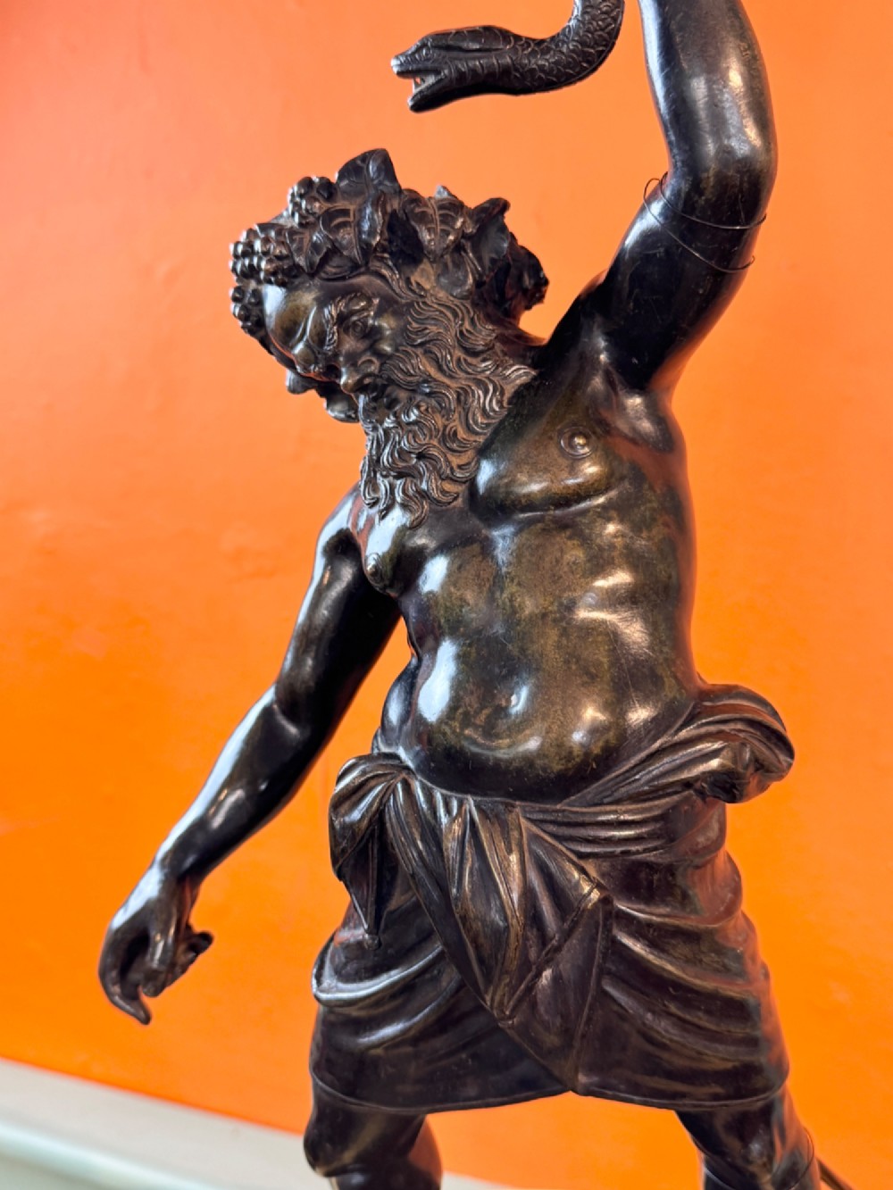 A dark patinated bronze sculptural table lamp depicting the classical figure Silenus holding a coiled serpent, set upon a carved circular base. View VI