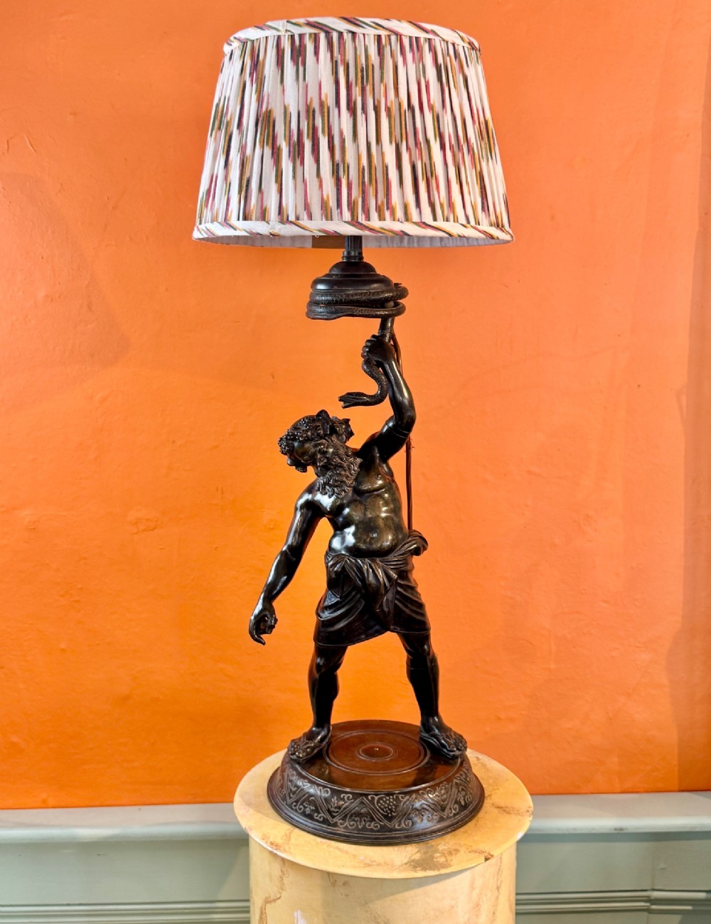 A dark patinated bronze sculptural table lamp depicting the classical figure Silenus holding a coiled serpent, set upon a carved circular base. View VIII
