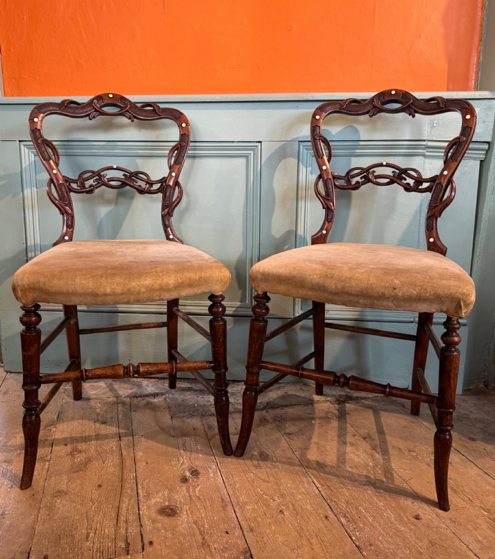 A pair of Victorian dark wood bedroom chairs with pierced scroll carved backrests, dot inlay, turned legs, and velvet seats.